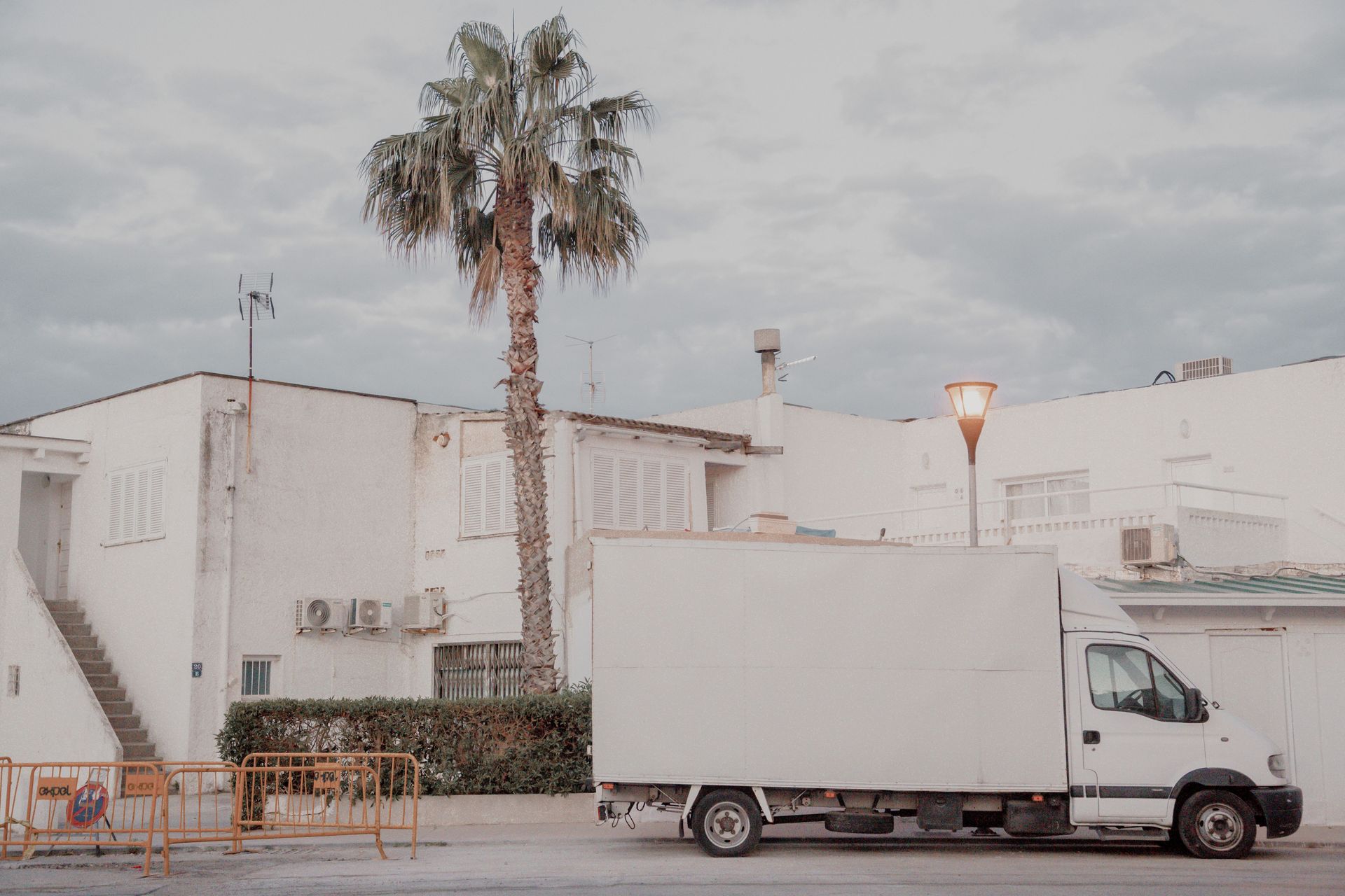 White delivery truck parked next to a white building with a palm tree in an urban setting.